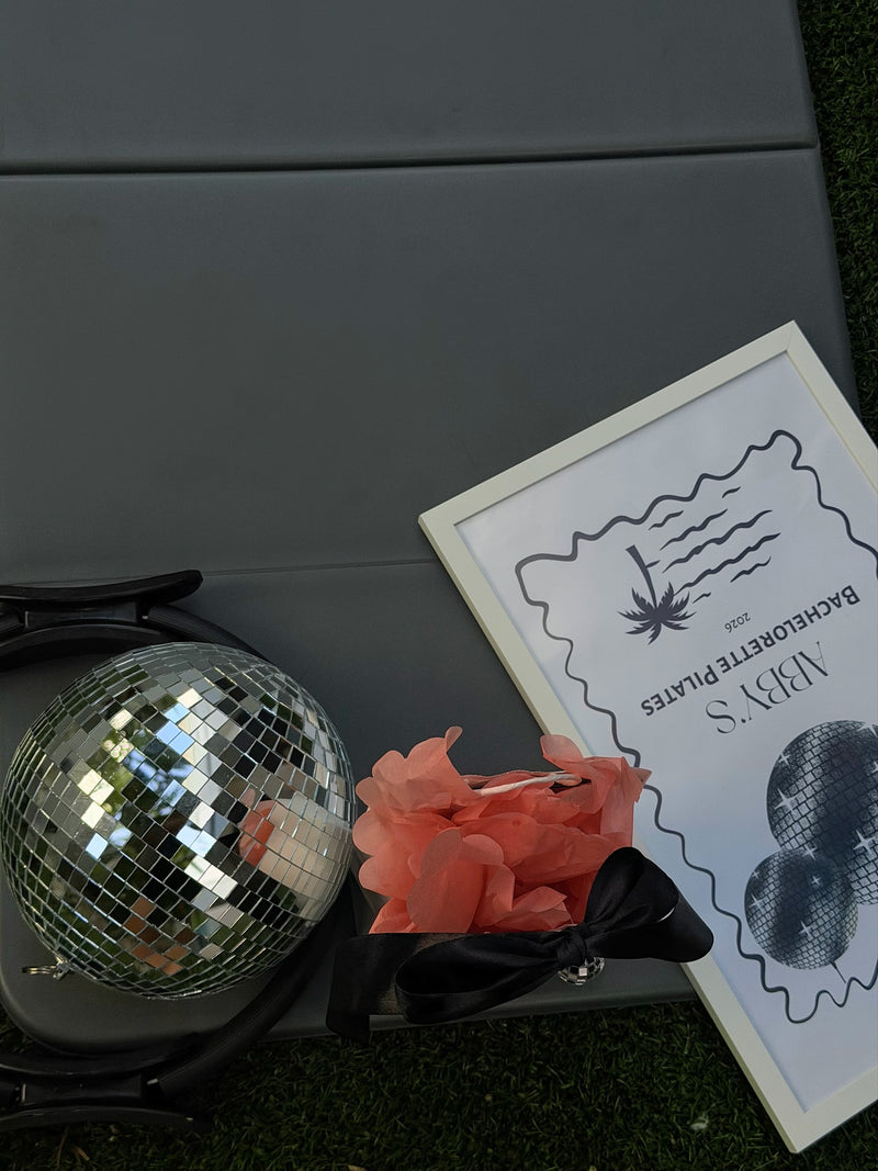 Disco ball, flowers and a custom Bachelorette Pilates sign laid out on a mat at a Club Sweat party