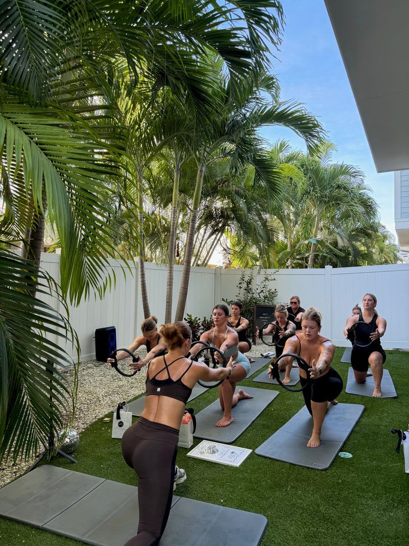 Bachelorette group doing a sculpt workout with Pilates rings on mats under palm trees in Tampa
